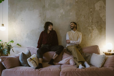 Happy multiracial gay couple talking while sitting on sofa at apartment