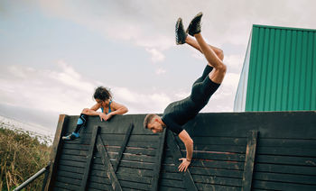 Friends jumping over wooden wall while exercising on land