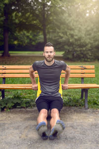 Portrait of smiling man doing push-ups on bench in park