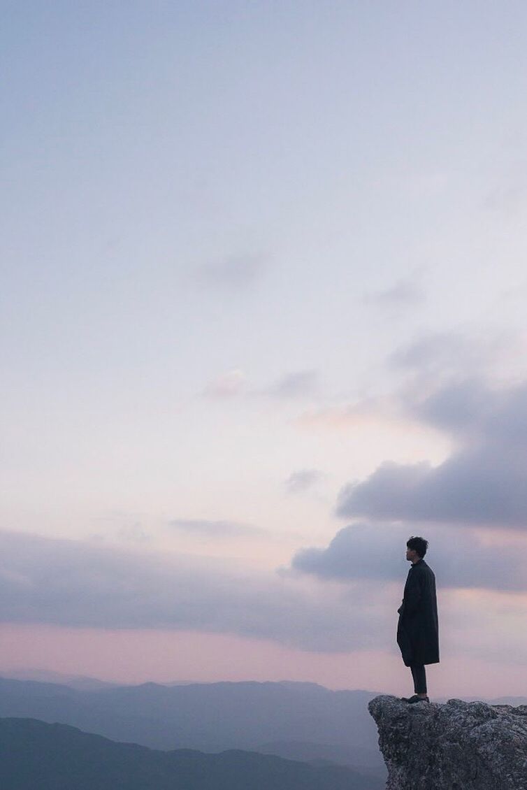 MAN STANDING BY MOUNTAIN AGAINST SKY