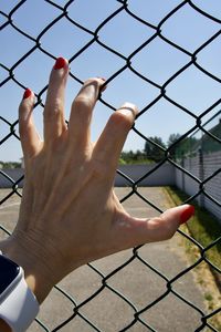 Low angle view of human hand on chainlink fence