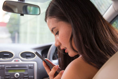 Close-up of young woman using mobile phone in car