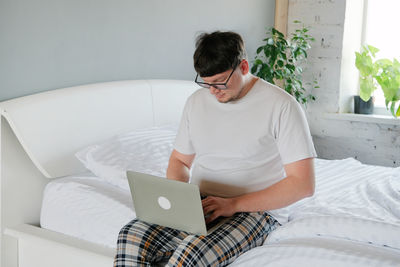 Man using laptop while sitting on bed at home