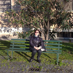 Portrait of young woman on bench against trees