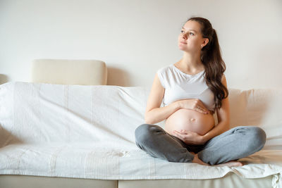 Young pregnant woman holding stomach sitting on sofa at home