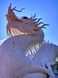 Low angle view of statue against blue sky and building