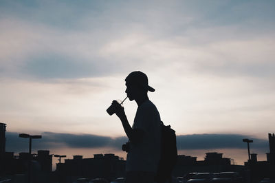 Silhouette man drinking coffee in city against sky