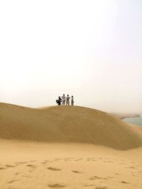 Men standing at desert against clear sky