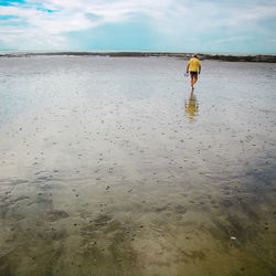 Rear view of man walking on wet beach