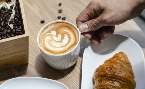 Cropped image of hand holding coffee cup on table