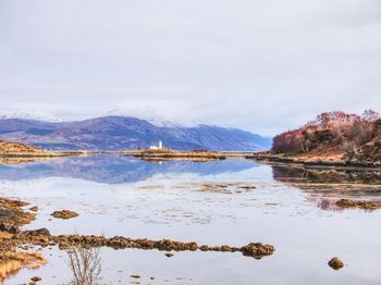 Isle ornsay with white tower of lighthouse.  scotland. sunny winter day with snowy mountains