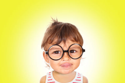 Portrait of girl sticking out tongue while wearing eyeglasses against yellow background