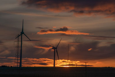 Silhouette wind turbines on land against sky during sunset