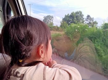 Rear view of girl looking through car window