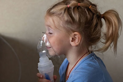 Little girl makes inhalation with a nebulizer at home, sitting on a chair. 