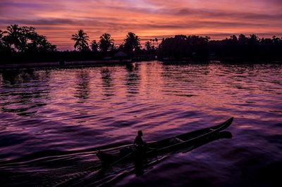 Man sailing boat in river against sky during sunset