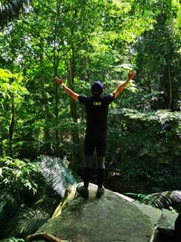 Full length rear view of man with arms raised standing in forest