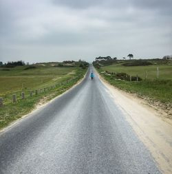 Empty road amidst grassy field against cloudy sky