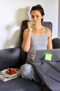 Young woman using mobile phone while sitting on sofa at home