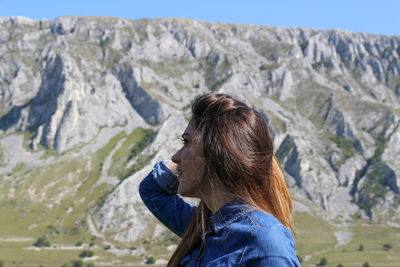 Side view of woman with hand in hair standing against mountains