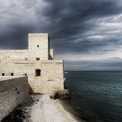 Buildings by sea against cloudy sky