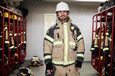 Portrait of confident male firefighter wearing protective uniform standing in locker room at fire station