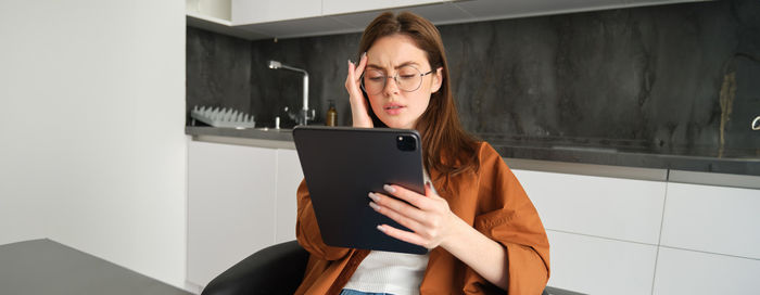 Young woman using digital tablet while standing against wall