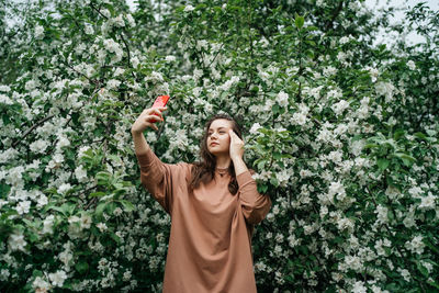 Girl in blooming apple tree using smartphone video call outdoor nature