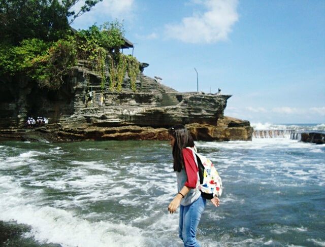 rock - object, day, water, sea, nature, outdoors, adults only, one person, adventure, one woman only, cliff, leisure activity, adult, vacations, waterfall, full length, architecture, people, beach, only women, standing, building exterior, wave, sky, beauty in nature, one young woman only, young adult