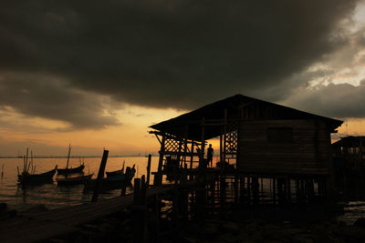 Boats moored by stilt house at dusk