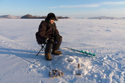 Woman - fisherman catches fish from the hole on a large frozen lake on the background of the island.