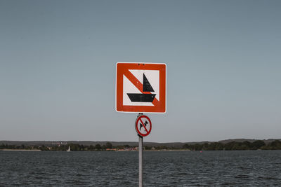 Road sign by river against clear sky