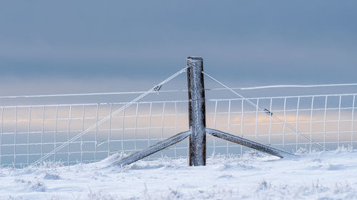 Fence on snow covered field against sky