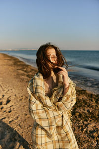 Portrait of young woman standing at beach against clear sky