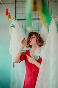 Thoughtful woman in red dress with curtain at home