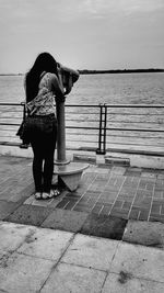 Rear view of woman standing on footpath by sea