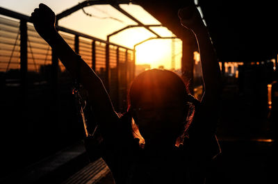 Silhouette girl with arms raised during sunset