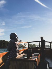 Rear view of man and woman standing by boat against sky