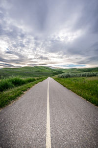 Road passing through field against cloudy sky