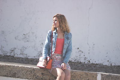 Young woman sitting against wall