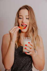 Portrait of beautiful young woman drinking water against wall
