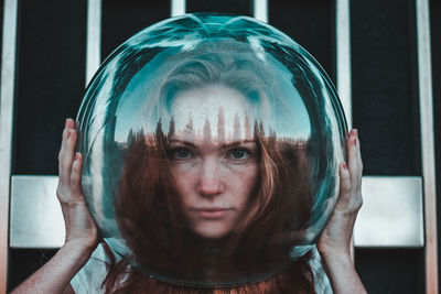 Close-up portrait of young woman wearing glass helmet in head against metallic railing