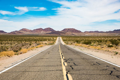 Empty road amidst desert against sky