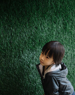 Cute boy standing against green plant