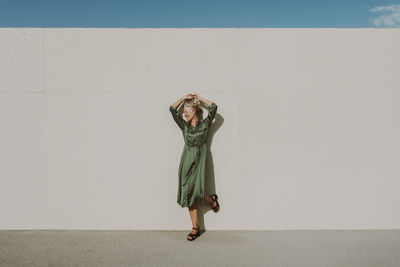 Smiling mature woman standing on one leg in front of white wall