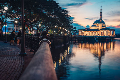 Man in illuminated city by river against sky