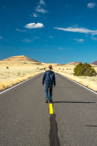 Rear view of man walking on road amidst field against sky