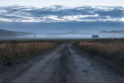 Dirt road amidst field against sky