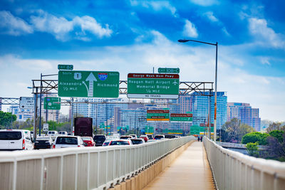 Road sign on bridge in city against sky