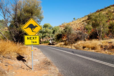 Road sign by trees against sky